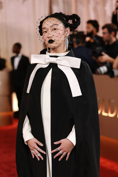 Audrey Nuna wears a black and cream cape with a bow and a black veil at the Golden Globes